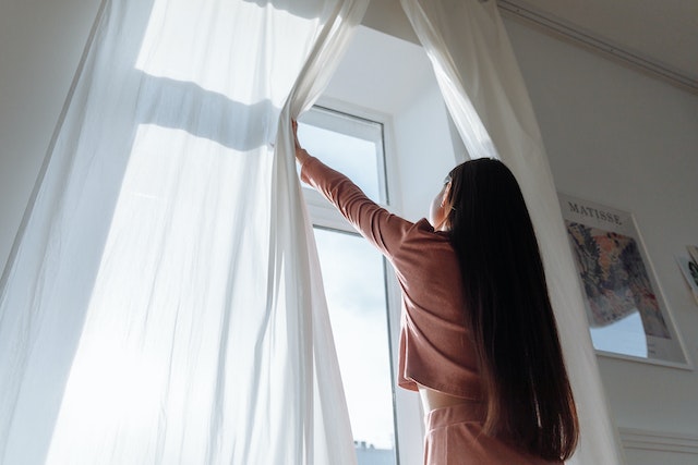 Person opening white window curtains